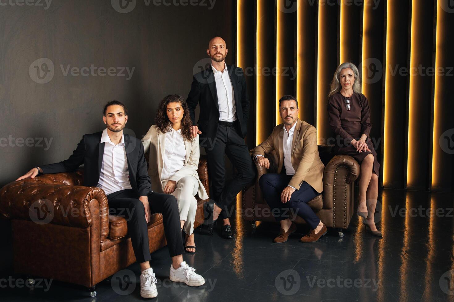 A group of five European executives stands in a stylish office environment. They are dressed in professional attire, showcasing teamwork and leadership qualities during a business meeting. photo