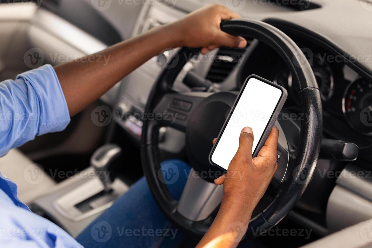 Over the shoulder view of happy black male driver holding smartphone with white blank screen, using mobile app for navigation, mock up. Closeup of cell phone with empty display, copy space template photo