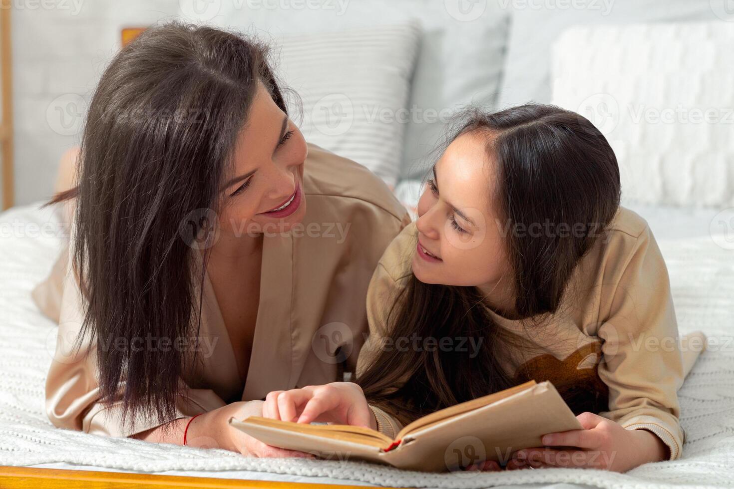 Family pastimes and activities. Caring young mother and her cute daughter reading book on bed at home. Adorable teen girl and her mum having quiet bonding times together, enjoying bedtime story photo