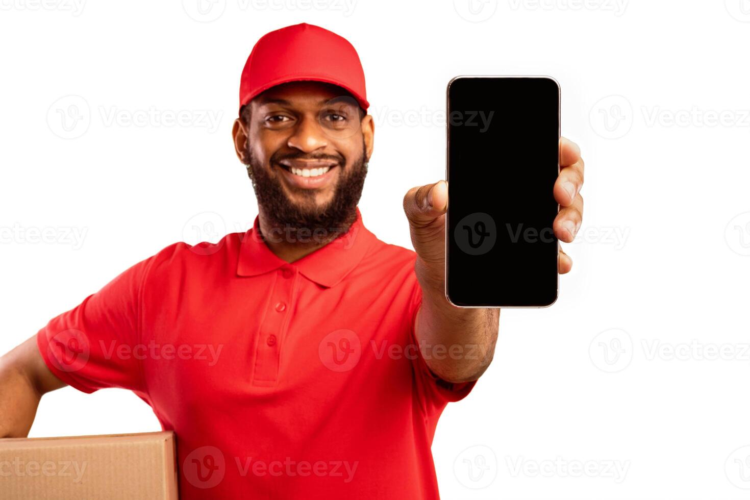Black Delivery Man Showing Smartphone Empty Screen Holding Cardboard Box Recommending Postal Express Shipping App Over Yellow Studio Background photo
