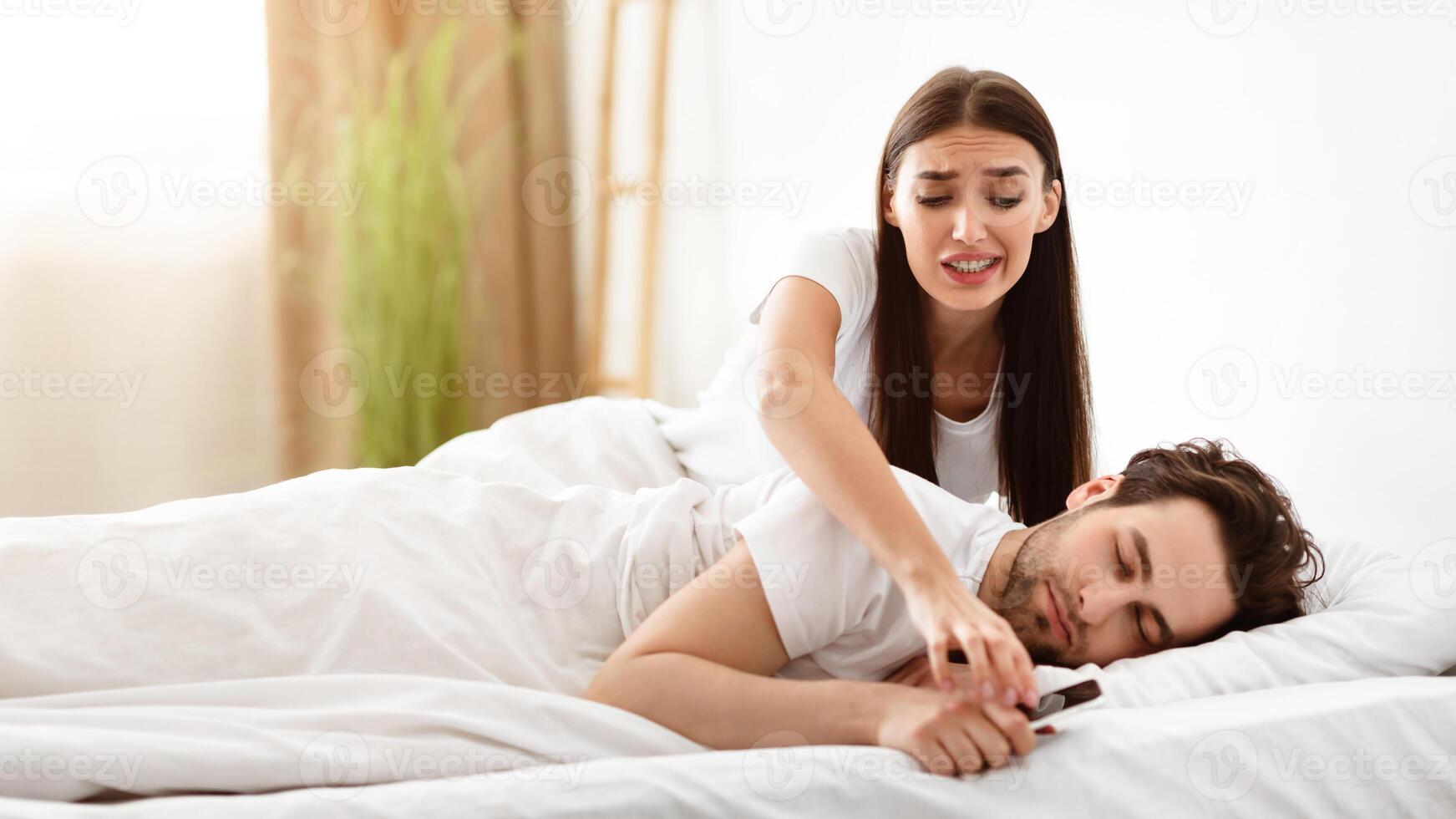 Jealous Girlfriend Checking Boyfriend's Phone And Messages Suspecting Affair While He Sleeping In Bed At Home. Jealousy And Mistrust Problem In Relationship. Selective Focus photo