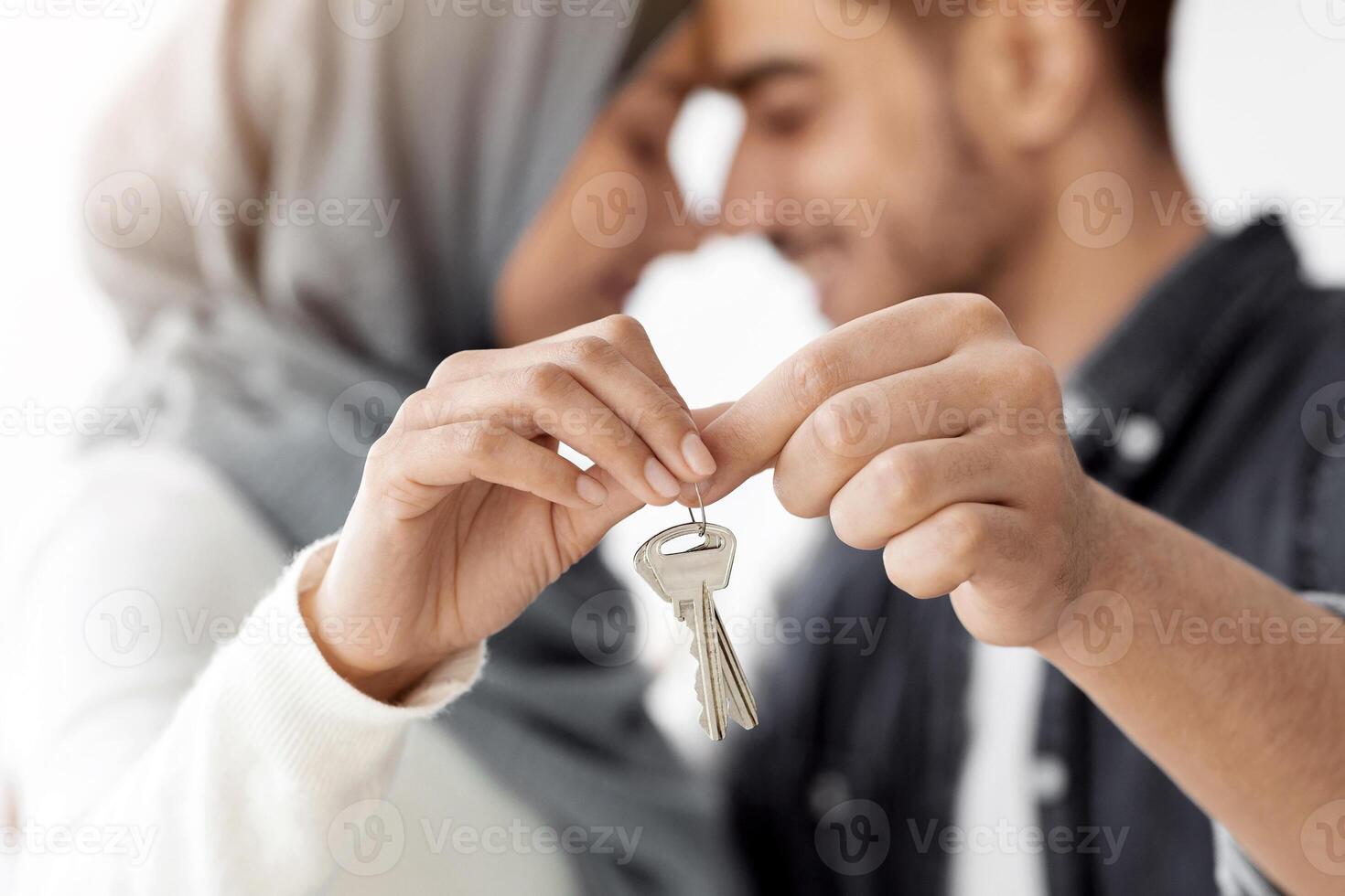 Closeup of key chain in loving muslim couple hands, selective focus. Happy middle-eastern family husband and wife showing key from their apartment, celebrating moving to new house photo