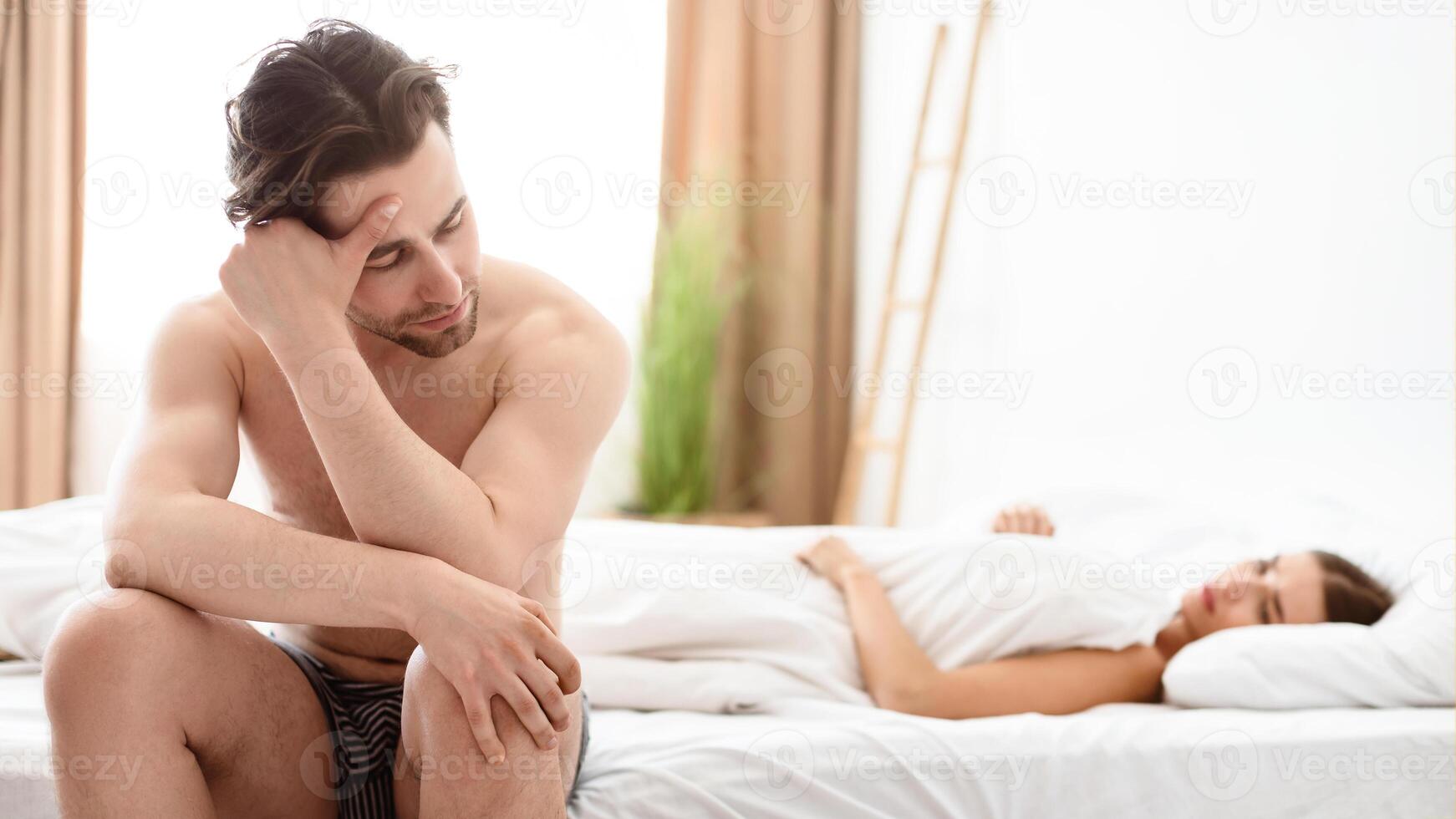 Erectile Dysfunction. Unhappy Man Having Erection Problems While His Girlfriend Lying In Bed In Bedroom At Home. Sexual Failure And Stress. Impotence, Male Health Issue. Selective Focus photo