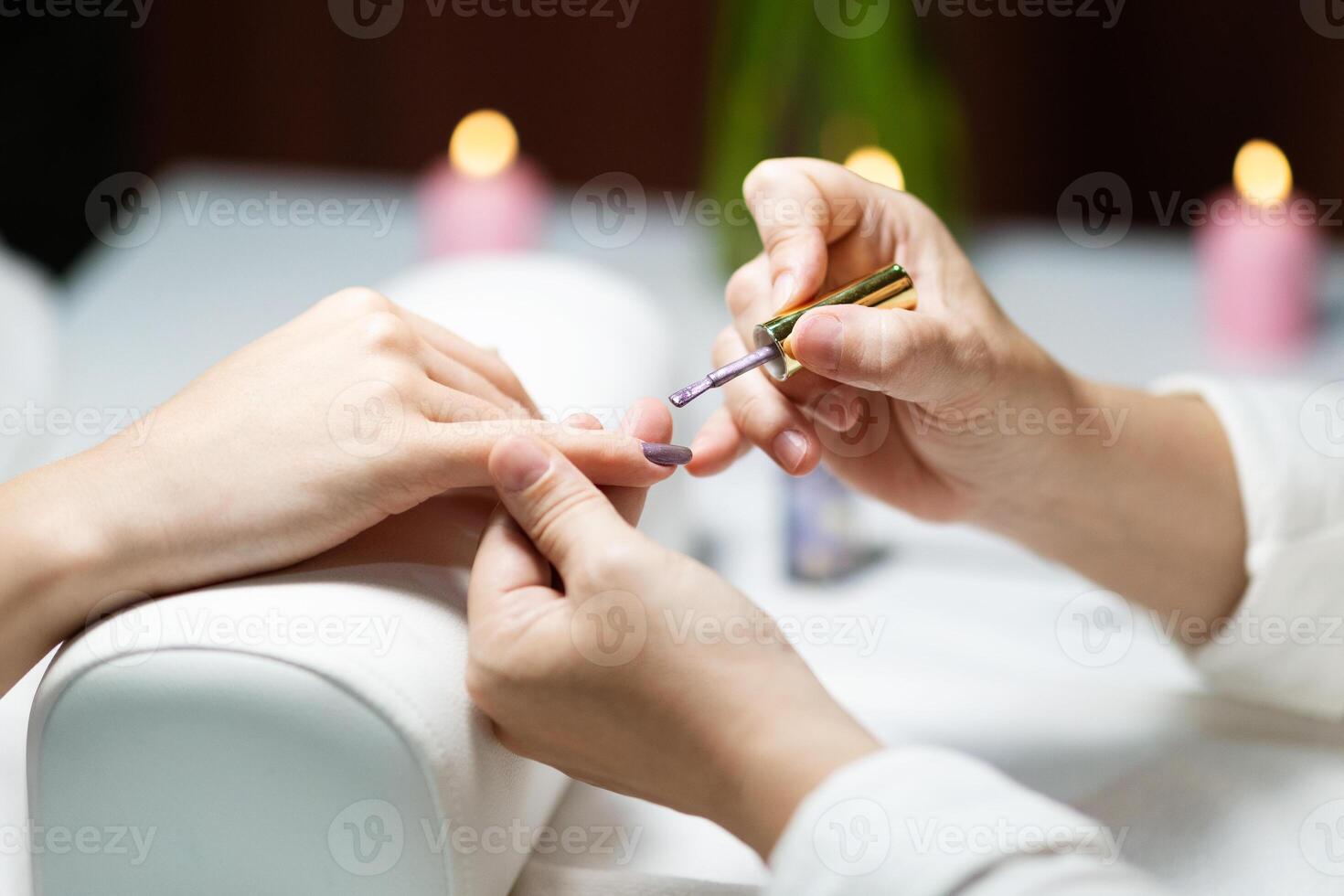 A skilled nail technician carefully applies nail polish to a client's nails in a serene beauty salon setting. The ambiance is enhanced with soft lighting from candles. photo