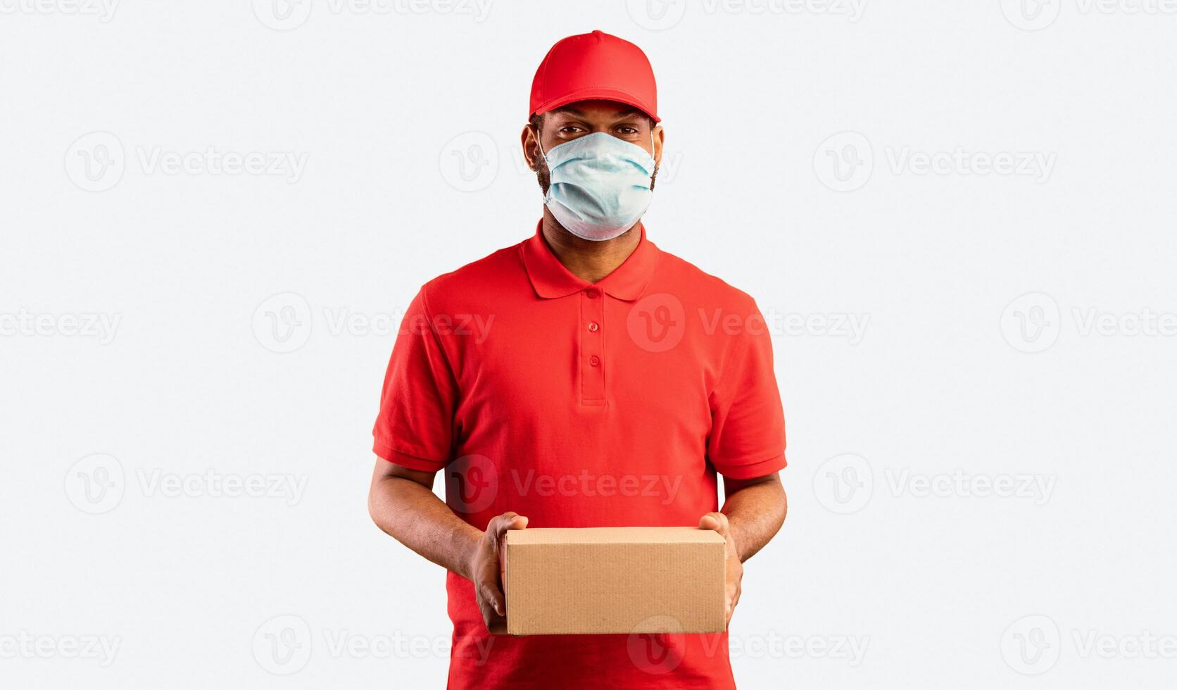 Delivery Service. African Courier Guy Holding Cardboard Box Delivering Parcel Package Wearing Protective Mask Posing Over Yellow Background. Studio Shot photo