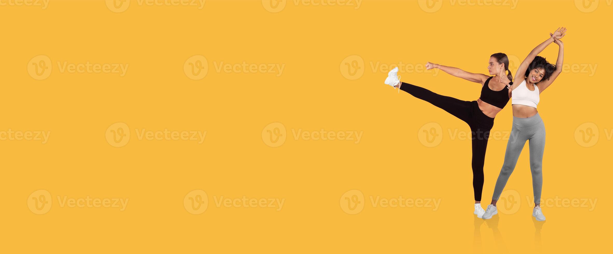 Two women are dancing cheerfully in stylish workout clothes, showcasing their energy and enthusiasm. The bright yellow background enhances the lively atmosphere of the moment. photo