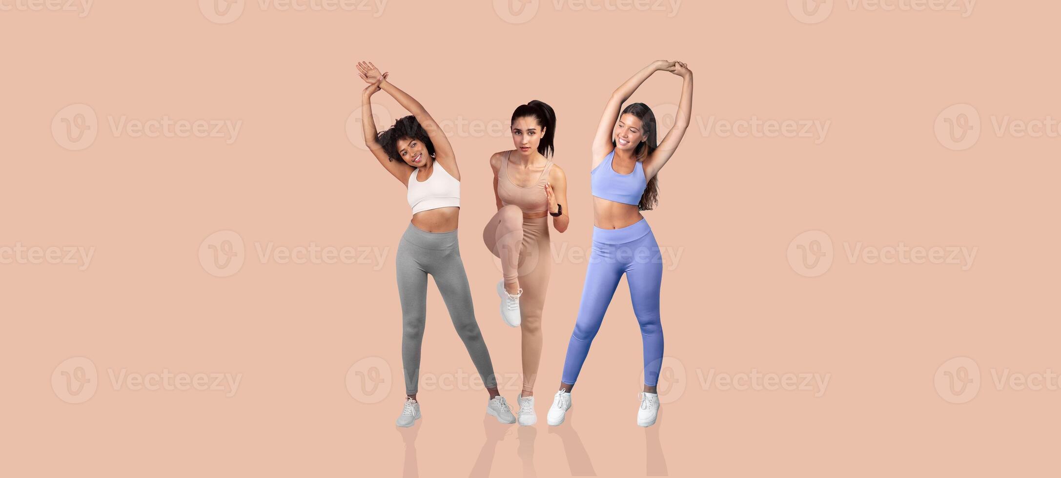 Three diverse women engage in a stretching routine indoors, showcasing different workout poses and vibrant athletic wear. The environment is bright and energetic, promoting fitness and well-being. photo