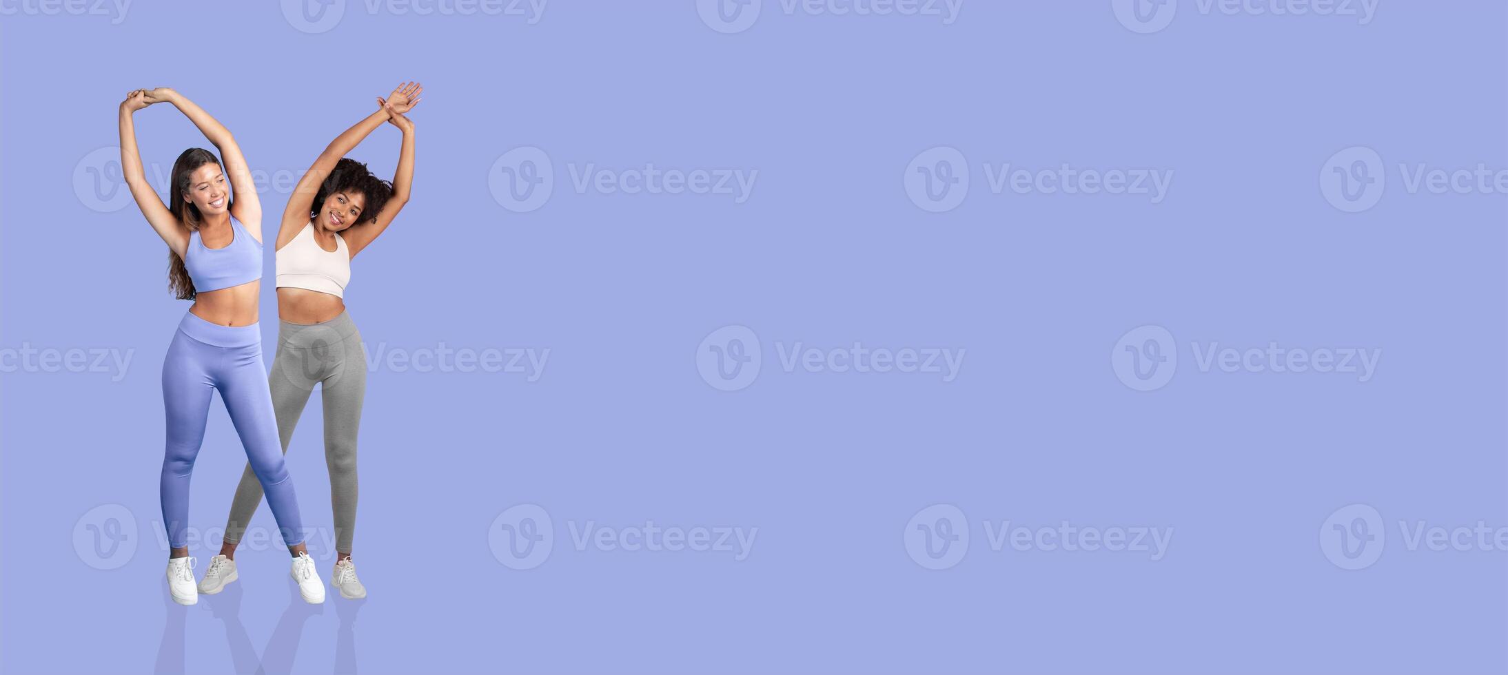 Two women engage in a stretching session, showcasing flexibility and fitness. They wear colorful workout gear and pose against a soft pastel background, highlighting a healthy lifestyle. photo