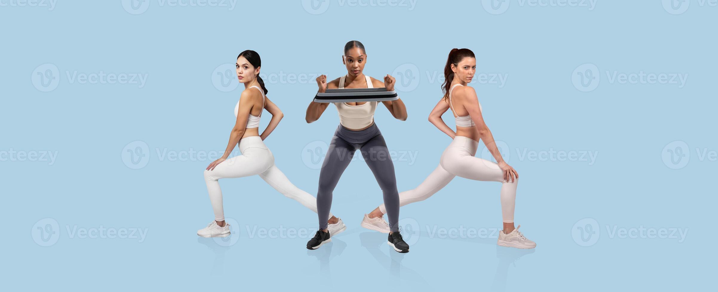 Three women are actively engaged in a workout, performing lunges and lifting weights in a bright, spacious fitness studio. The atmosphere is focused and energetic. photo