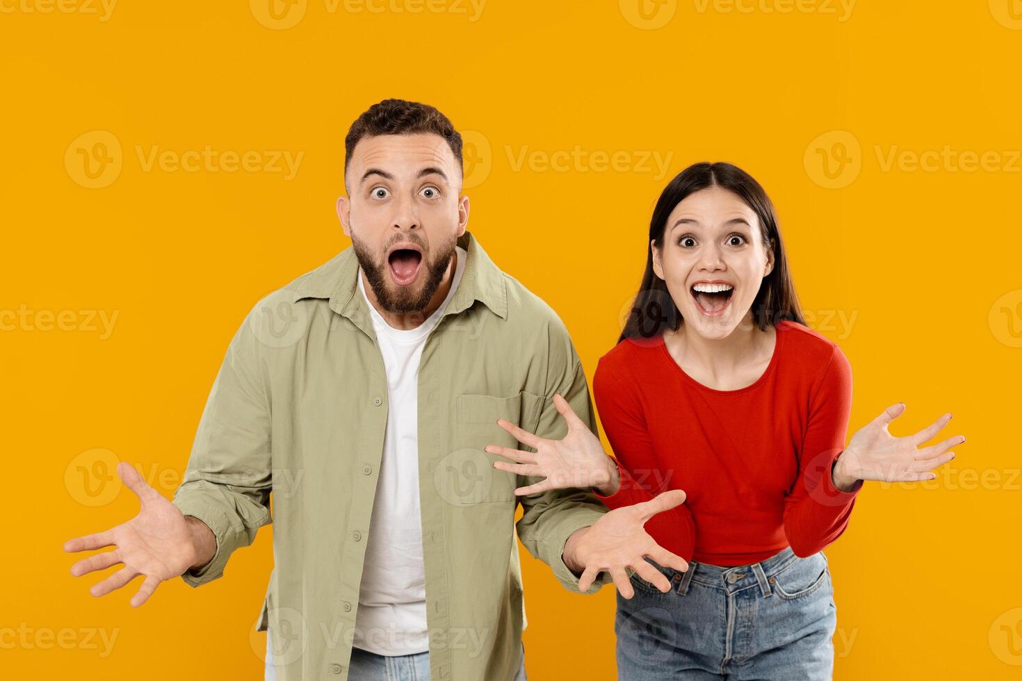 A joyful couple stands against a bright yellow background, both with wide smiles and surprised expressions. They are excited and share a moment of happiness and connection. photo