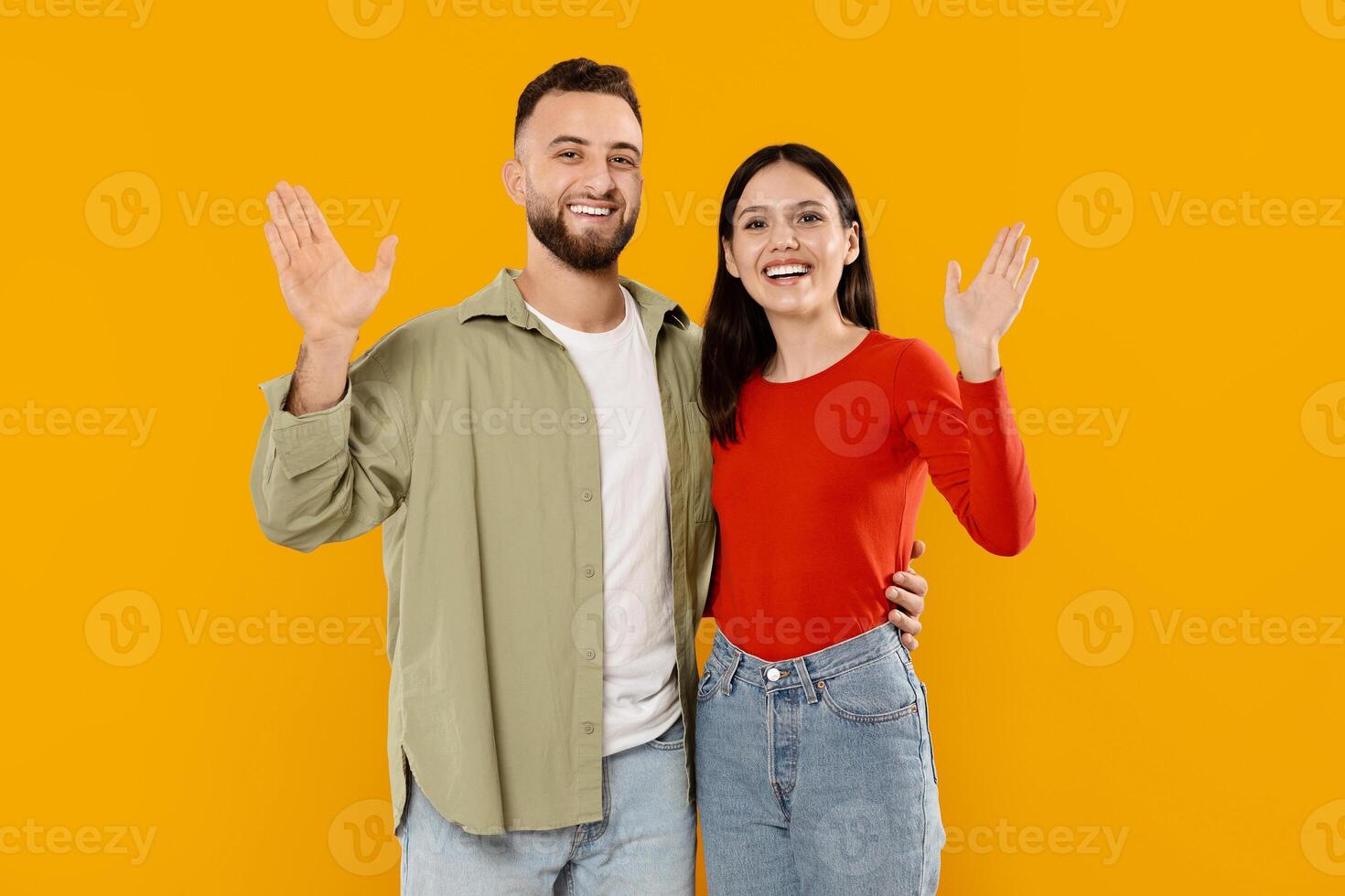 Young married couple smiles and waves at the camera while standing close to each other. Their warmth and affection shine through as they celebrate their love together. photo
