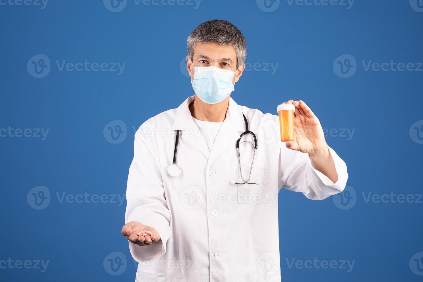 A middle aged Caucasian man, dressed in a white coat and mask, displays a prescription bottle while extending his other hand. He appears focused and ready to assist in a healthcare environment. photo