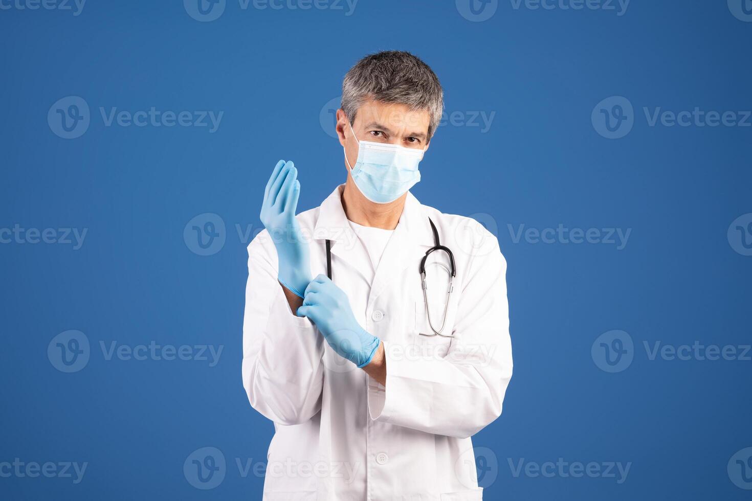 European doctor wearing a medical mask and gloves is getting ready to provide care. He is focused and ready for patient interaction in a clean, isolated environment. photo