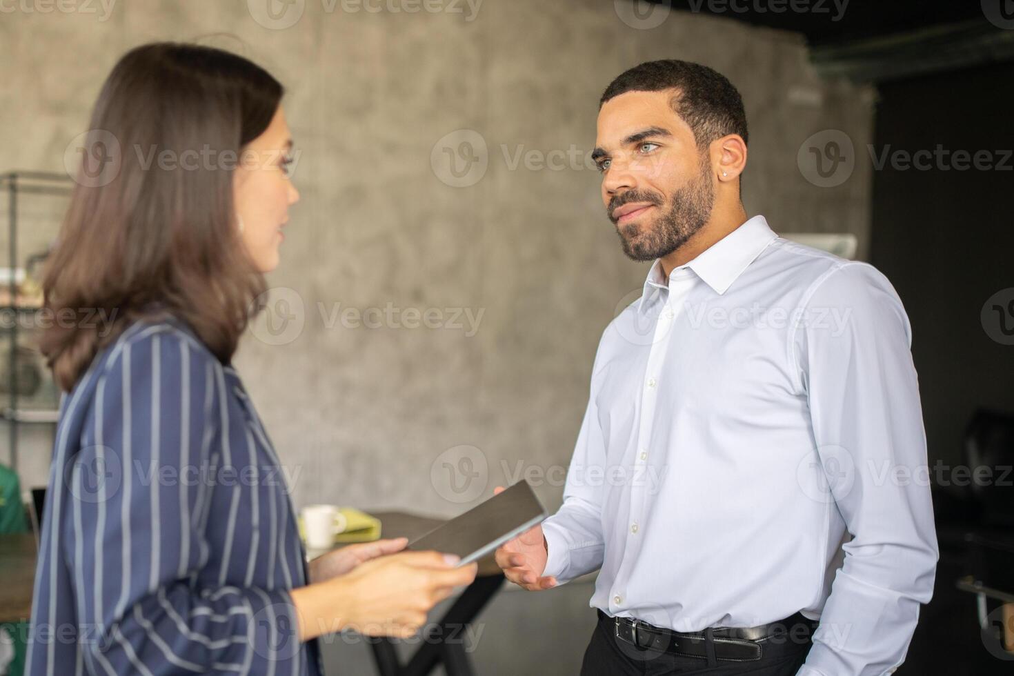 Two professionals engage in a productive discussion at a modern office. They exchange ideas and materials in a collaborative atmosphere, exemplifying teamwork and cooperation in their careers. photo