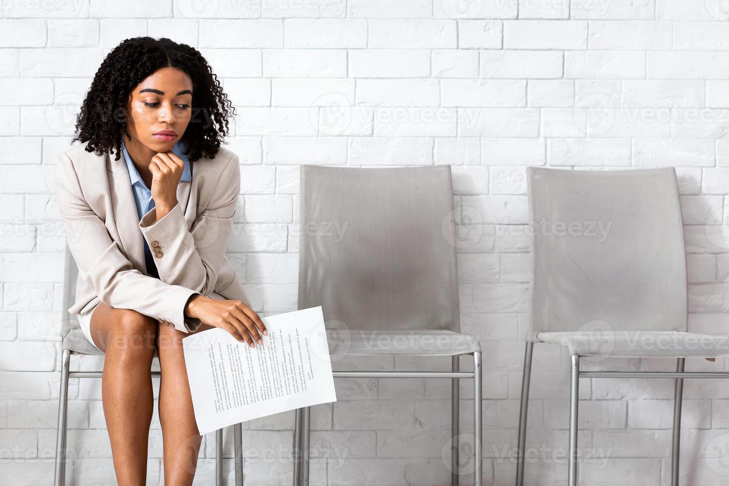 Bored black woman with CV tired of waiting for employment interview at office lobby, free space. Female vacancy candidate applying for job at multinational company. Work search and headhunting concept photo