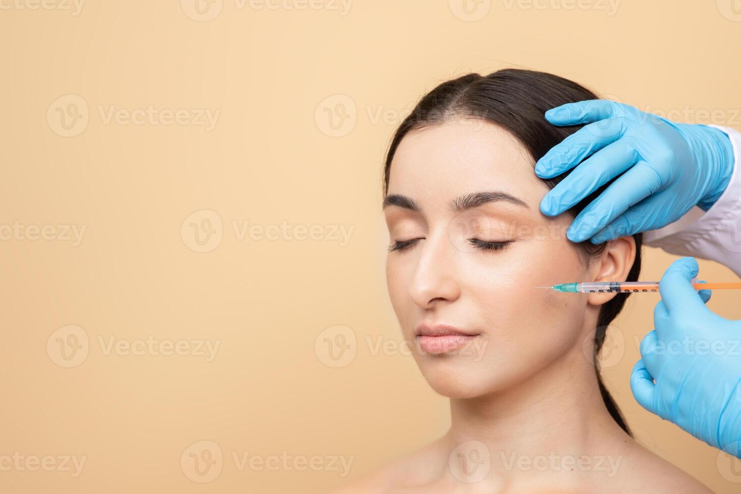 A young European woman with brunette hair relaxes as a professional applies a skin care treatment. The setting features a warm, neutral background, copy space photo