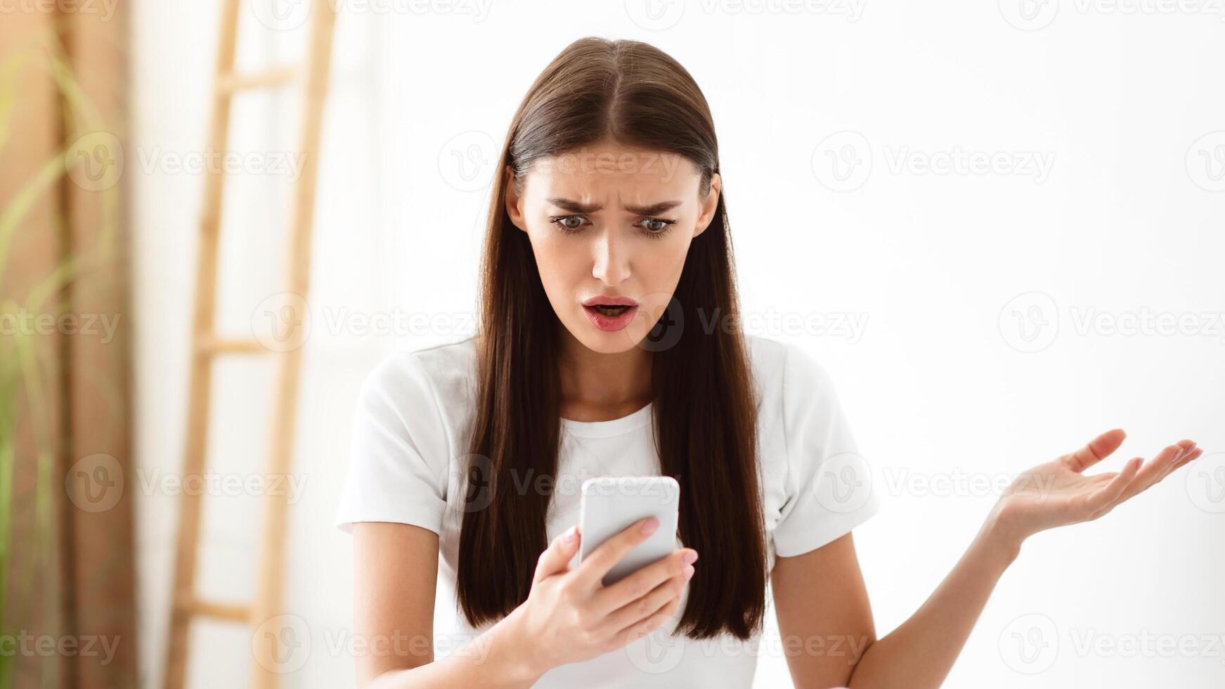 Jealousy And Infidelity. Shocked Girlfriend Holds Cheating Boyfriend's Phone And Reads His Messages From Lover While He Sleeps In Bedroom At Home. Betrayal In Relationship Concept. Selective Focus photo