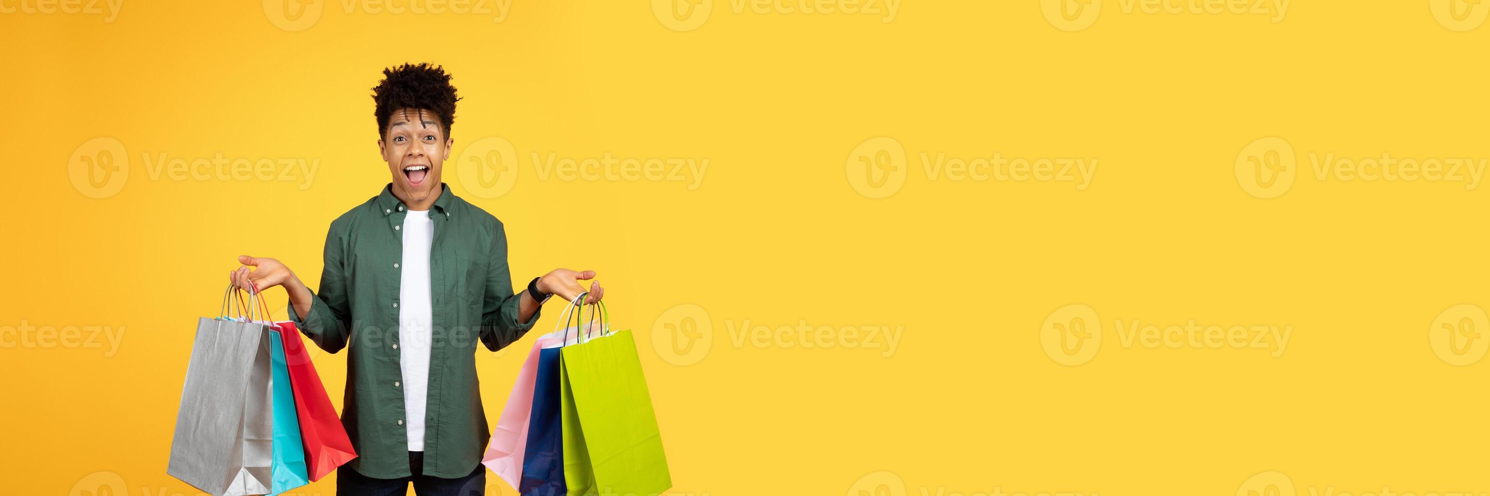Surprised and happy young black man holding several shopping bags with a cheerful look, copy space photo