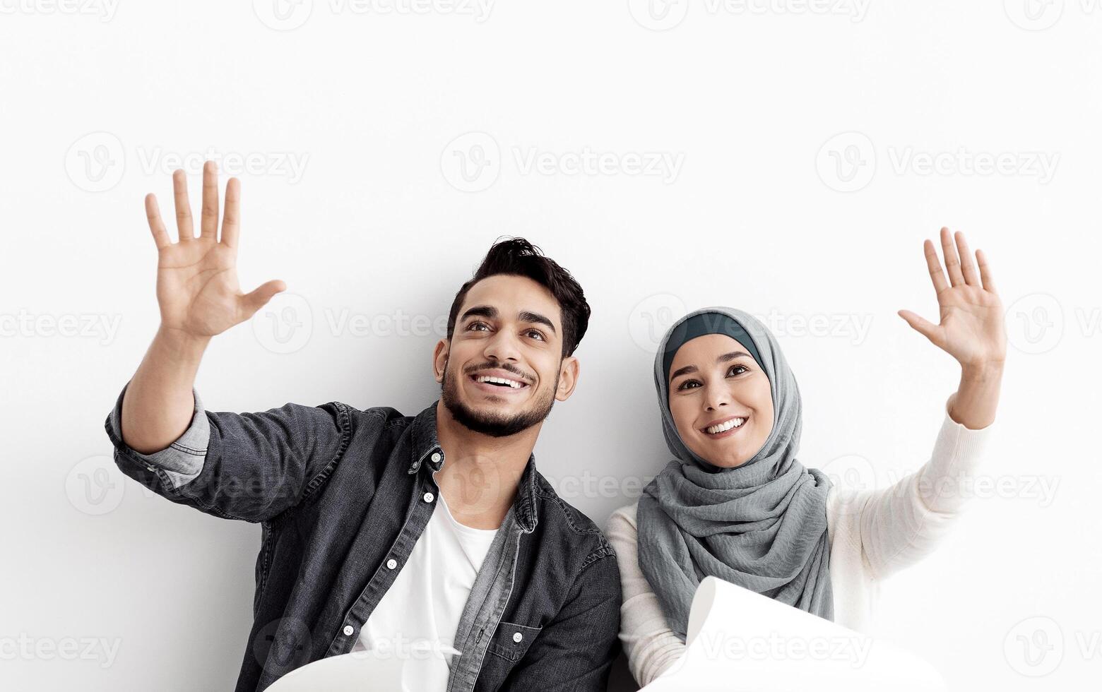 Loving muslim couple thinking about design in their new house, sitting on floor over white empty wall, holding apartment plan and imaging future interior. House design, interior, planning concept photo