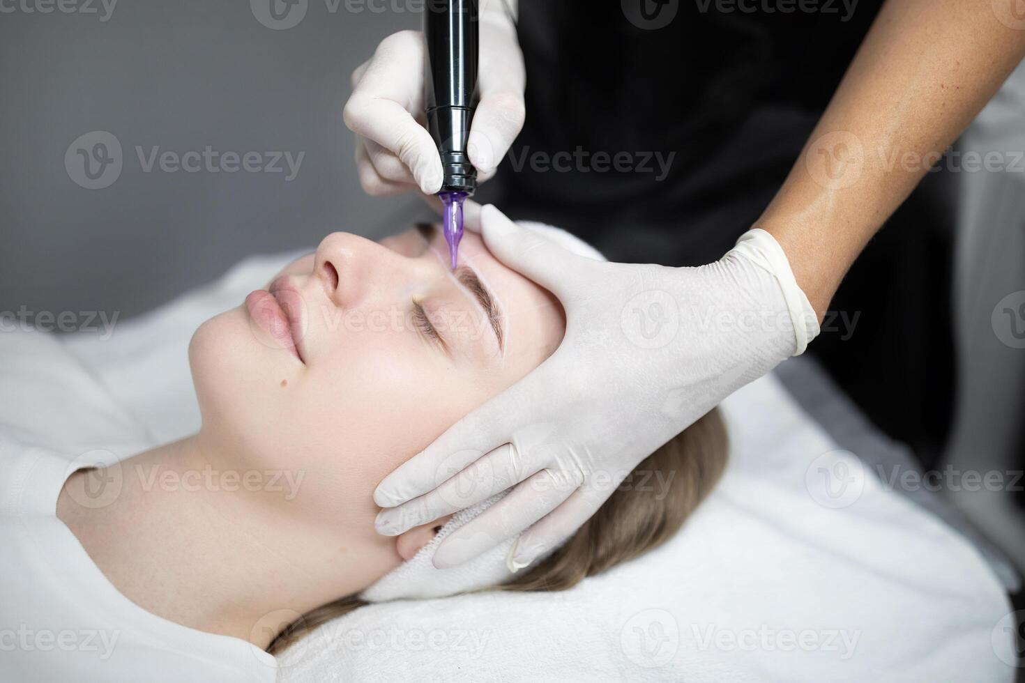 A client relaxes in a modern salon as a technician carefully applies permanent makeup to enhance her eyebrows. The setting promotes beauty and pampering through expert services. photo
