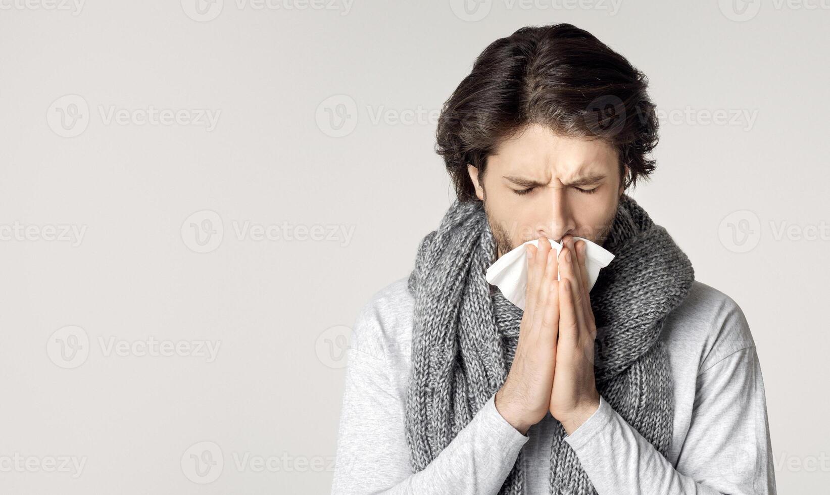 Guy with scarf around his neck, feels sick, sneezes in napkin photo