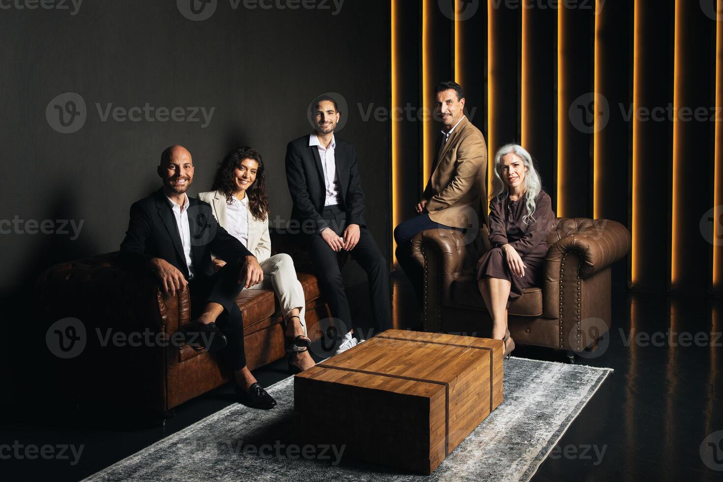 A group of European business professionals is gathered indoors, engaged in discussion. The modern office features stylish leather seating and warm lighting, creating a professional ambiance. photo