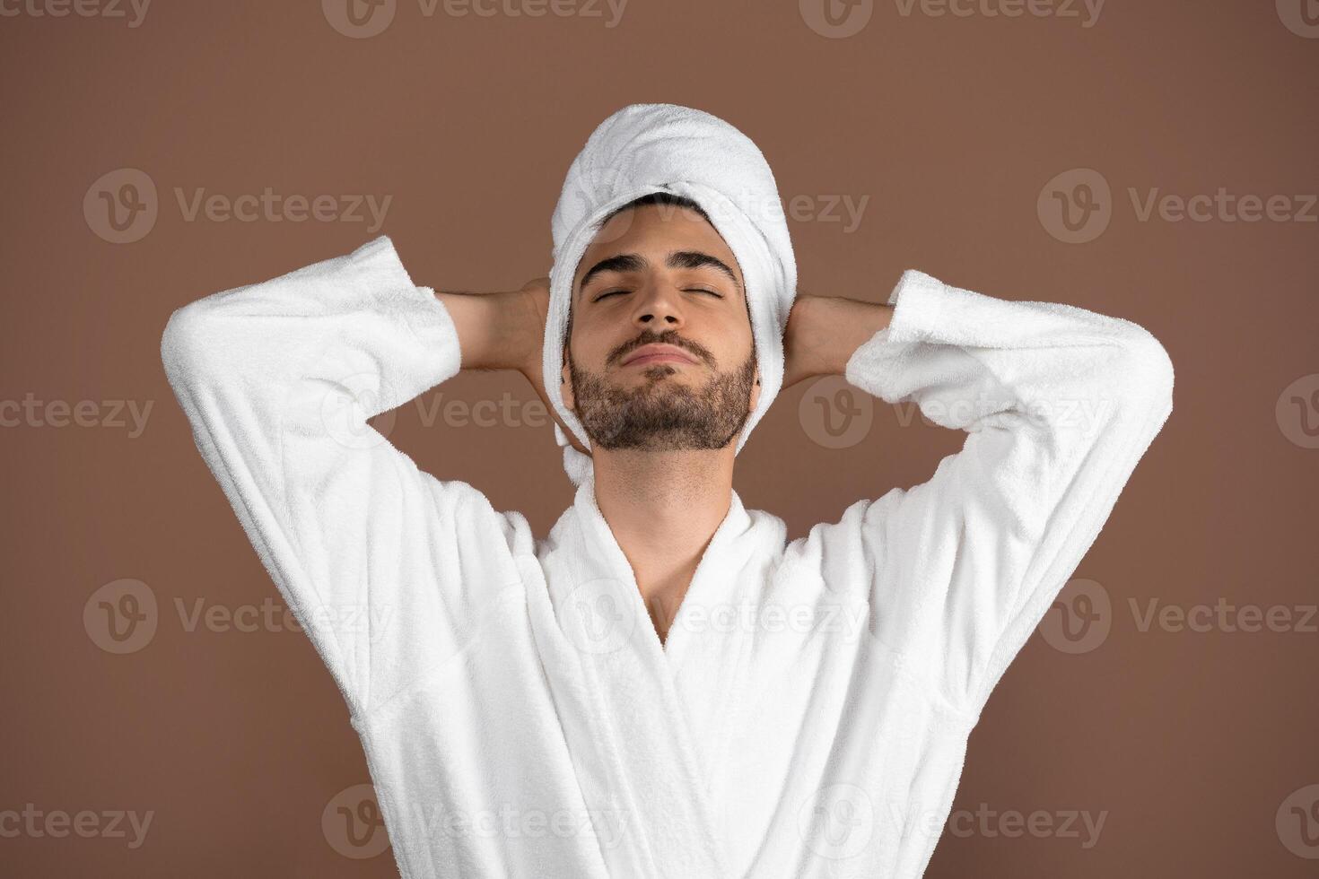 A young Caucasian man with curly hair relaxes in a cozy setting. He wears a soft robe and towel, embodying a lifestyle of self-care and tranquility. The ambiance exudes relaxation. photo