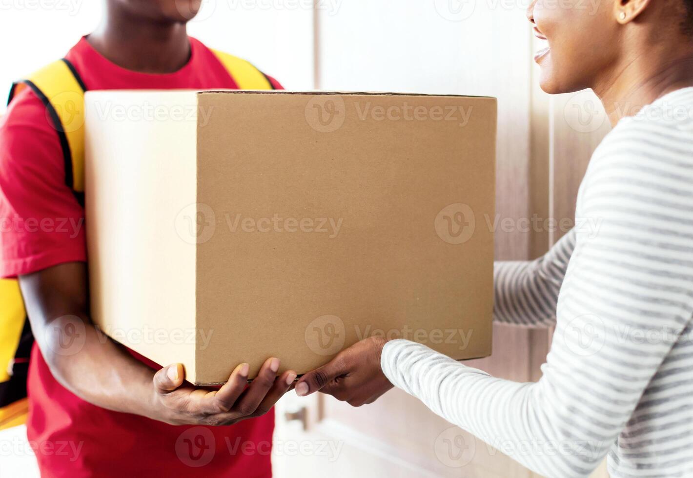 Professional Courier In Uniform Delivering Parcel To African American Lady Customer, Giving Her Paperboard Box Standing In Doorway Of Her Home. Package Delivery Concept. Cropped, Selective Focus photo