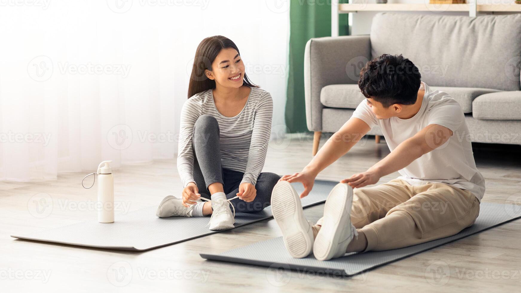 Cute asian young couple exercising together at home, positive korean man and woman in sportswear sitting on fitness mat, stratching and having conversation, copy space. Healthy lifestyle concept photo