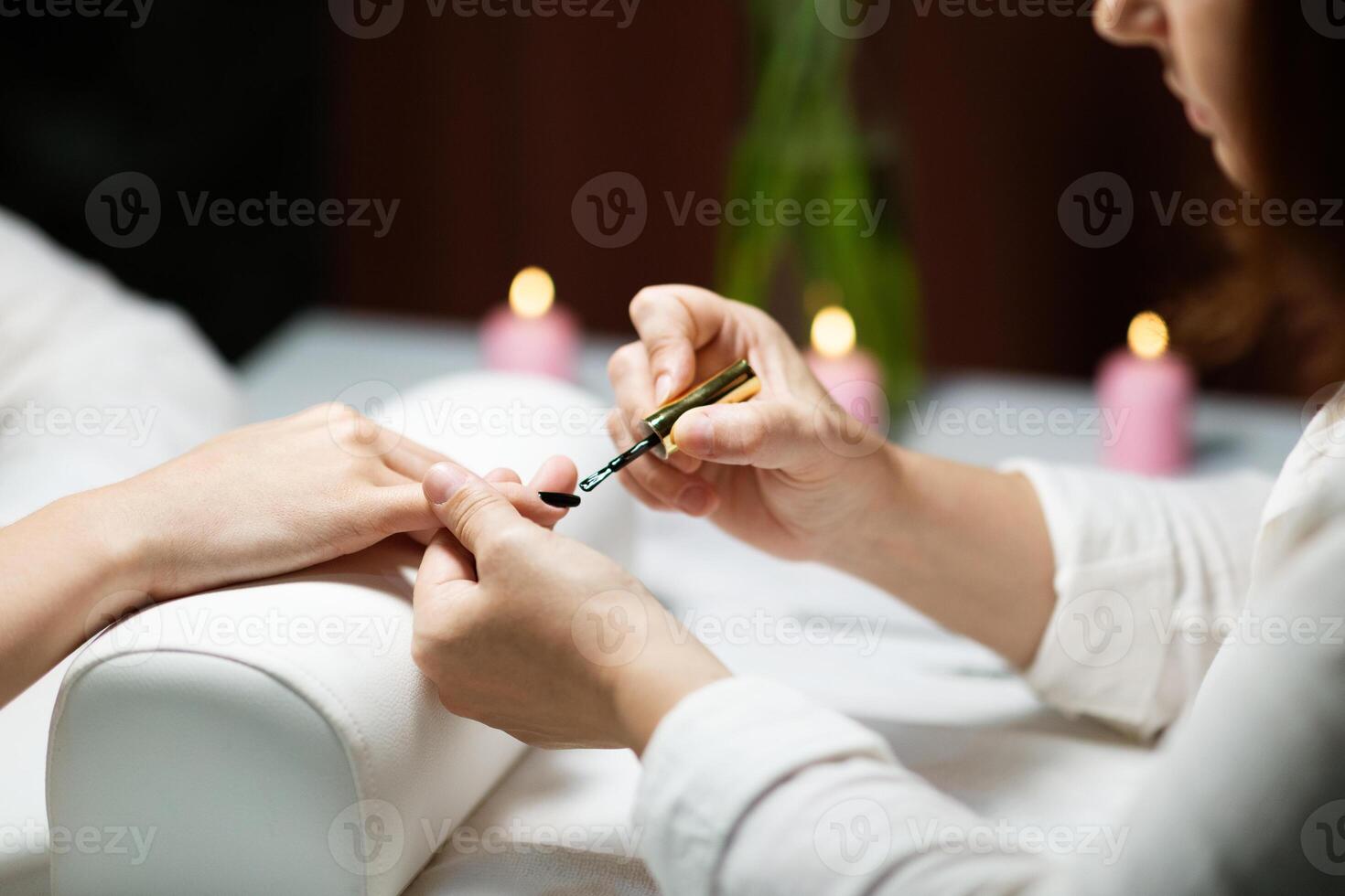 In a relaxing salon setting, a woman enjoys a manicure treatment while having her nails pampered. Soft candlelight creates a serene atmosphere for beauty care. photo