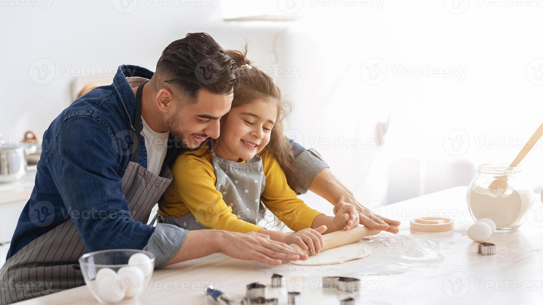 Arab dad and little daughter rolling up dough for cookies on table in kitchen while baking at home, middle eastern father and cute female kid making pastry together, enjoying cooking, copy space photo