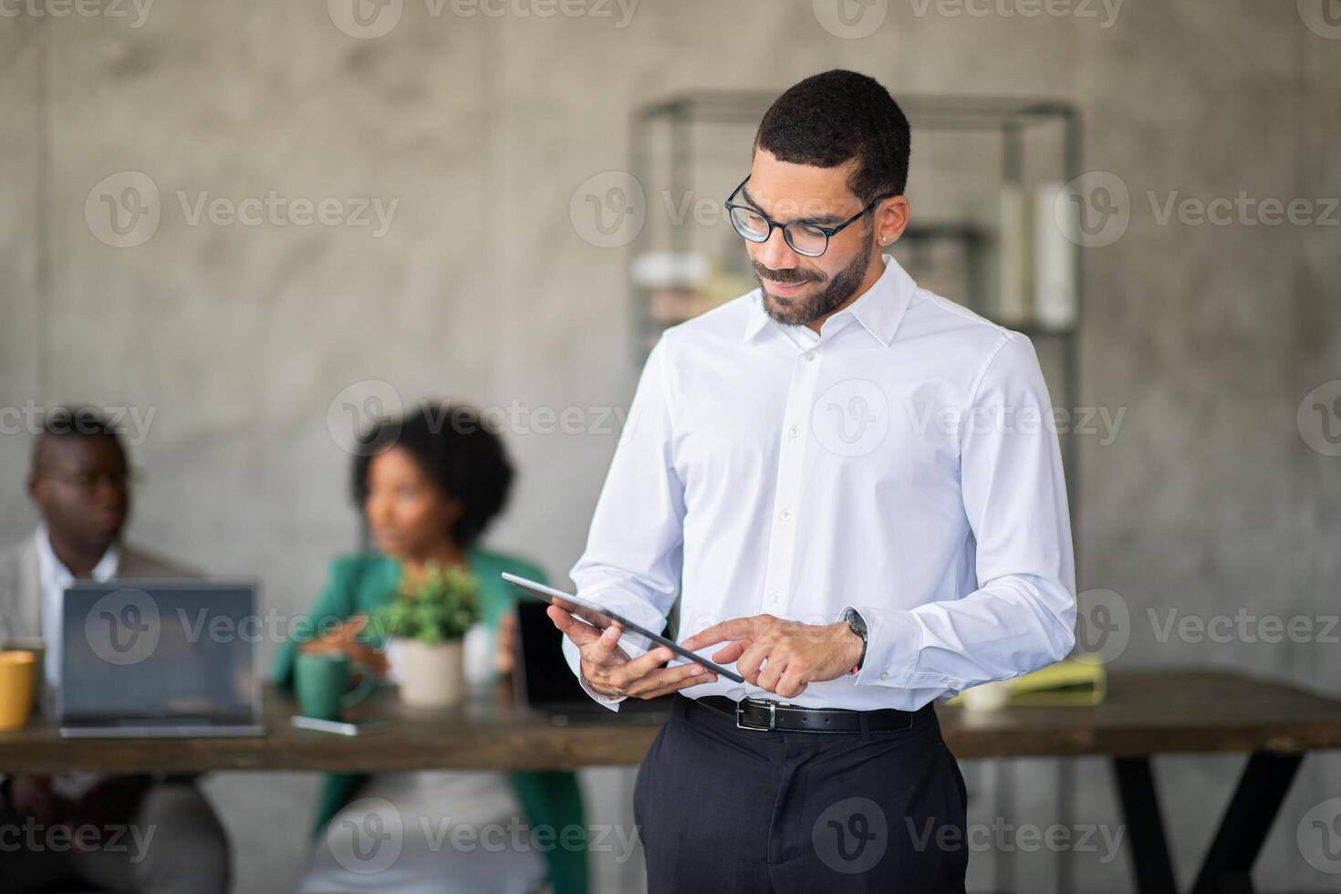 A group of professionals engage in a productive meeting in a contemporary office space. One member uses a tablet while others discuss, showcasing teamwork and collaboration. photo