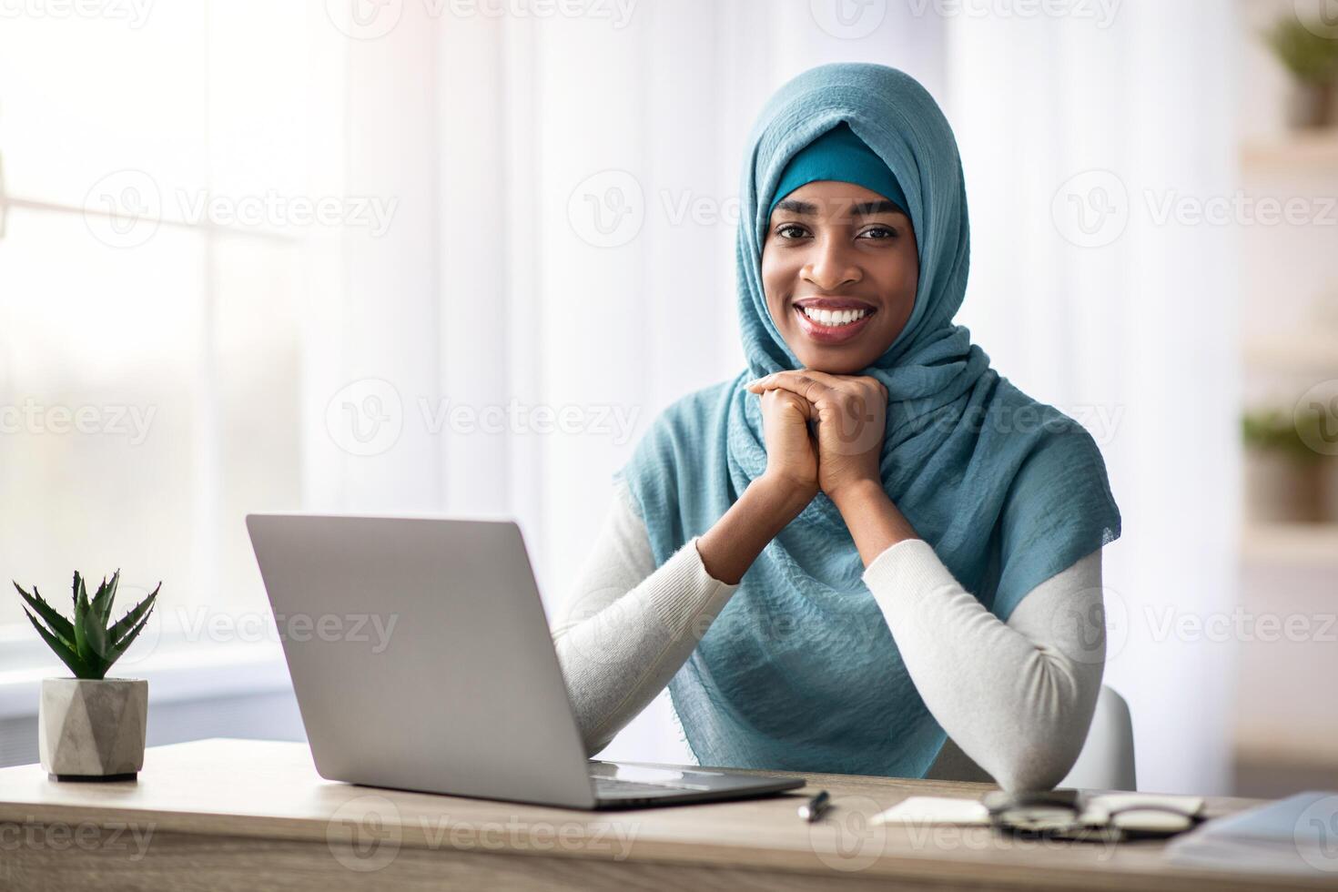 Portrait Of Happy Smiling Black Muslim Lady In Hijab Sitting At Desk With Laptop, Cheerful Young Islamic Freelancer Woman Posing At Camera While Working With Computer At Home Office, Copy Space photo