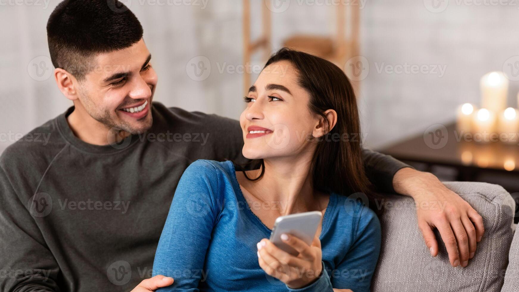 Happy Family Concept. Young lovely couple embracing and using smart phone, sitting on couch at home photo