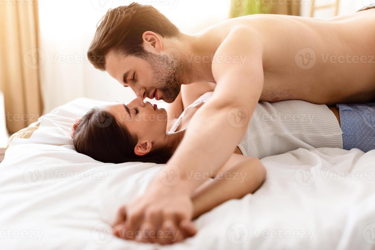 Passionate Couple Kissing Holding Hands Lying In Bed Making Love And Enjoying Intimacy In Modern Bedroom. Millennial Spouses Having Sex Enjoying Sensual Foreplay. Selective Focus photo