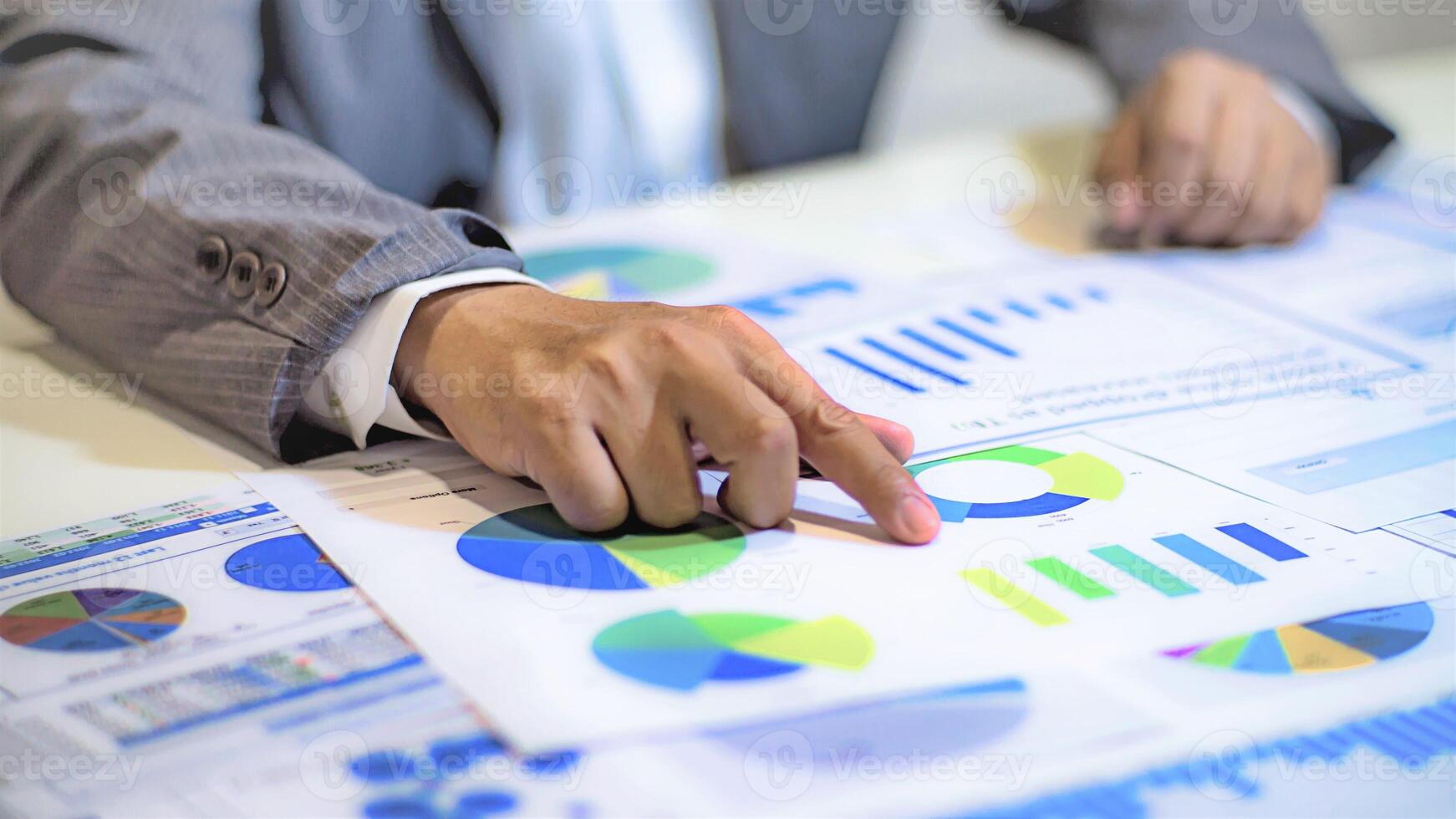 A person in a suit is pointing at graphs on a table photo