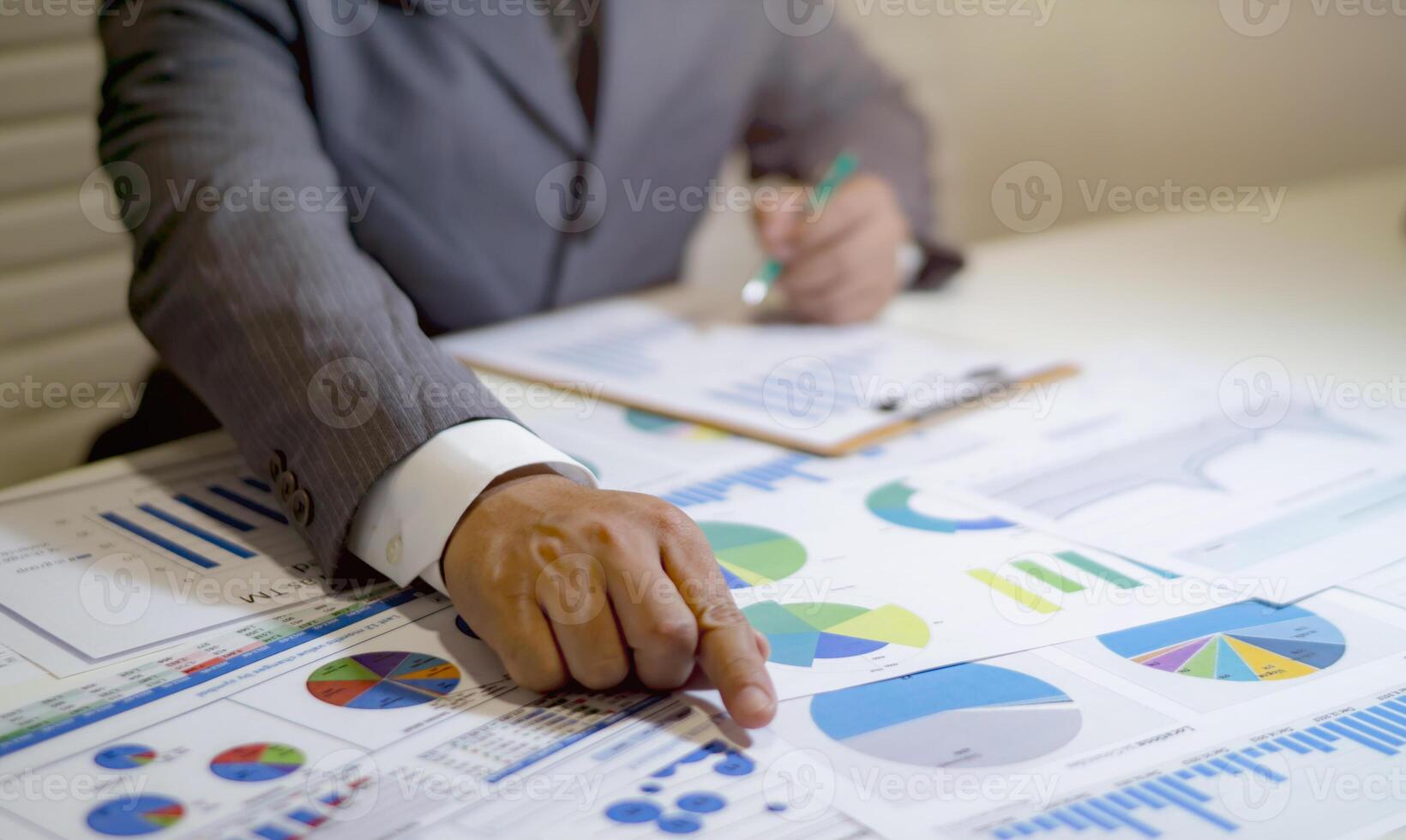 A man in a suit is pointing at graphs on a table photo