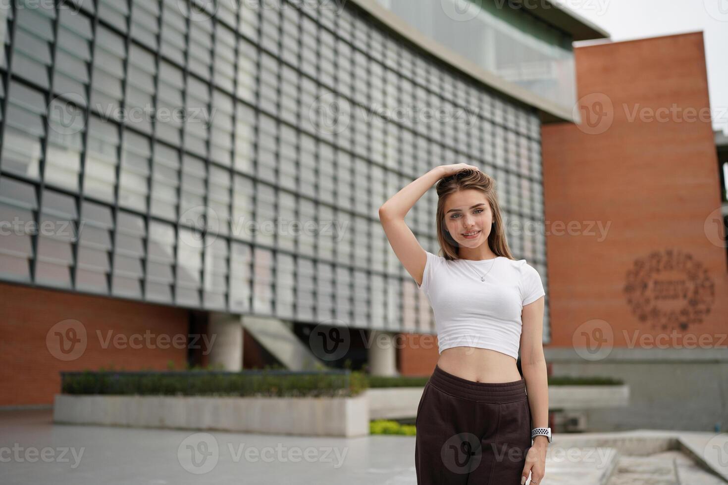 A woman in a white top and brown pants posing in front of a building photo
