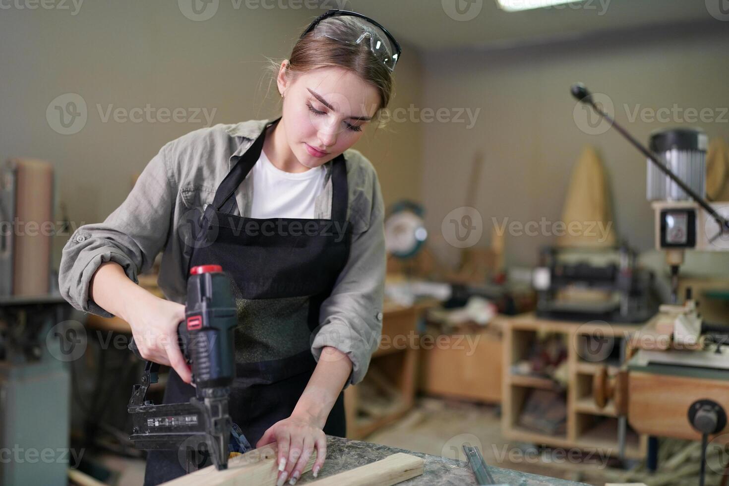 A woman in an apron is using a drill to make a piece of wood photo