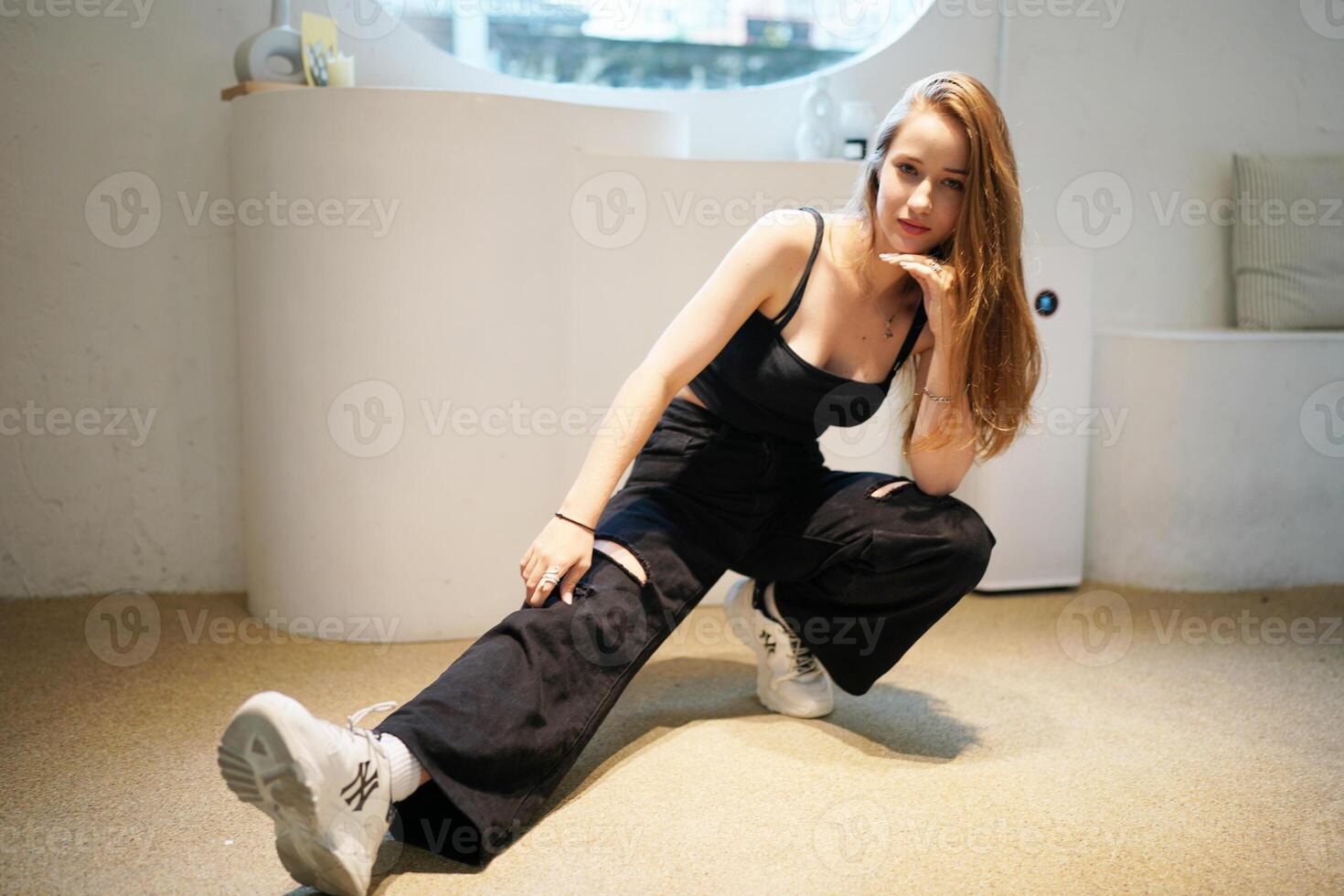 A woman in black pants and sneakers kneeling on the floor photo