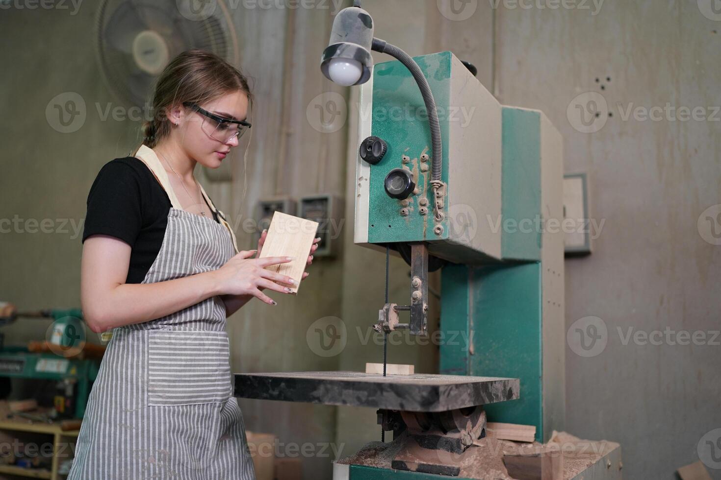 A woman in an apron is working on a piece of wood photo