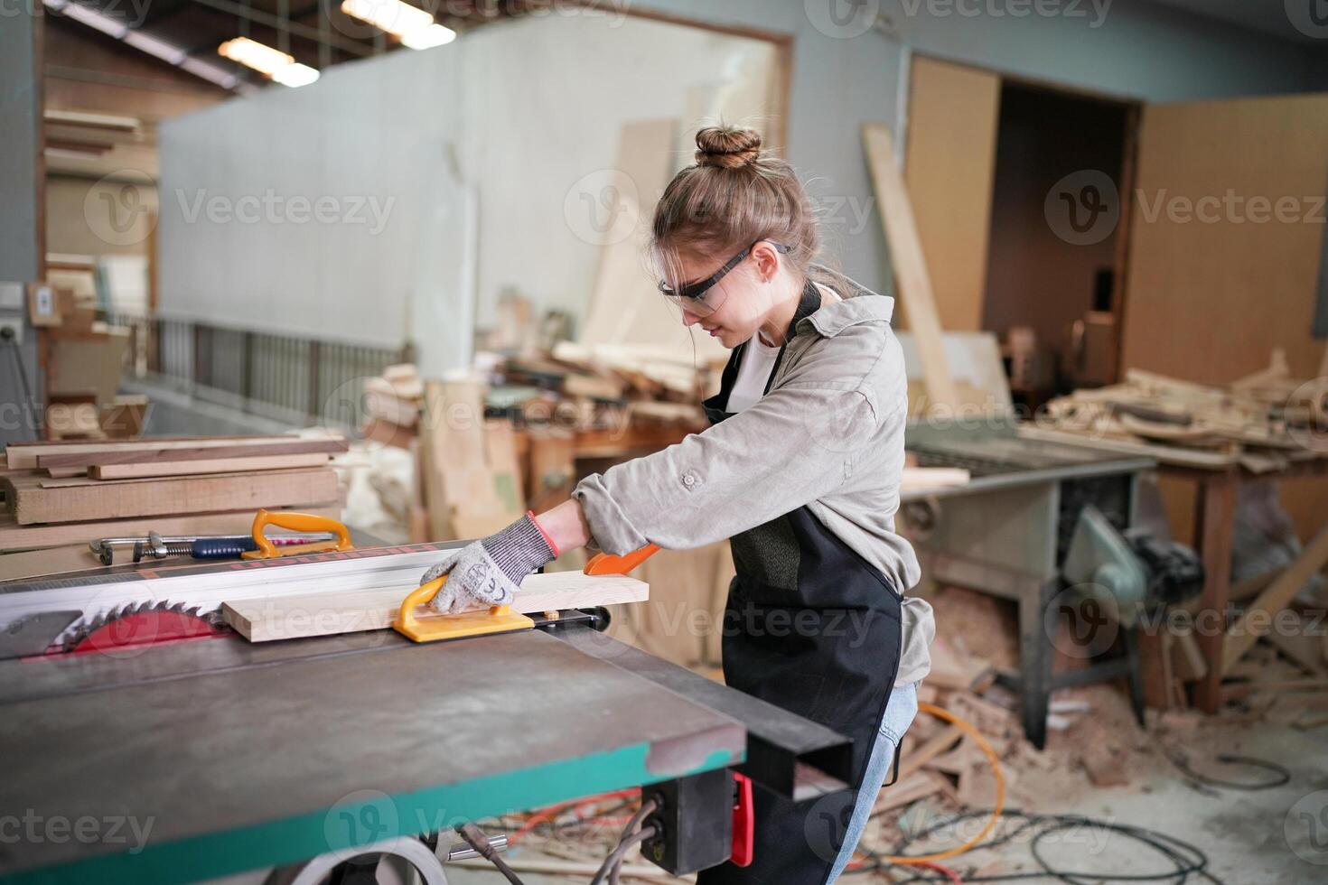 A woman is working on a table saw in a wood shop photo