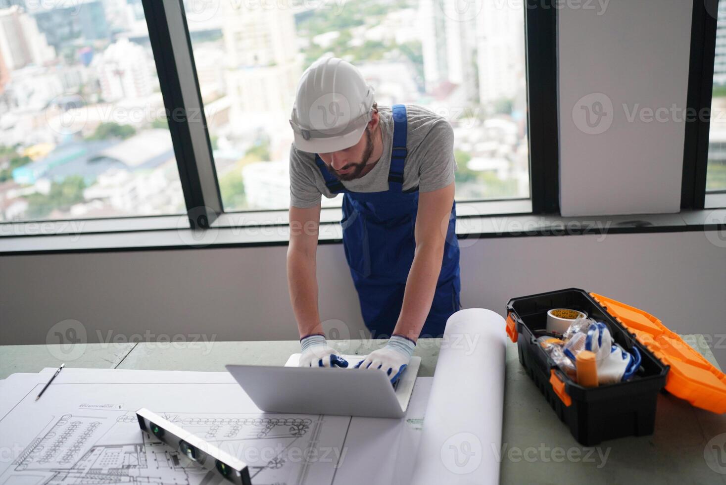 A man in a hard hat and blue shirt working on a laptop photo