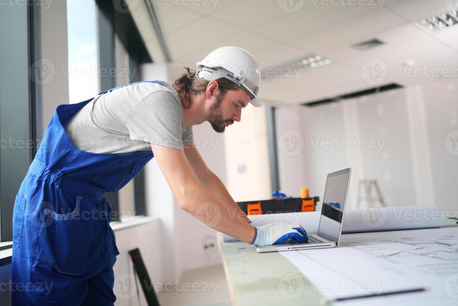 A man in blue overalls working on a laptop photo