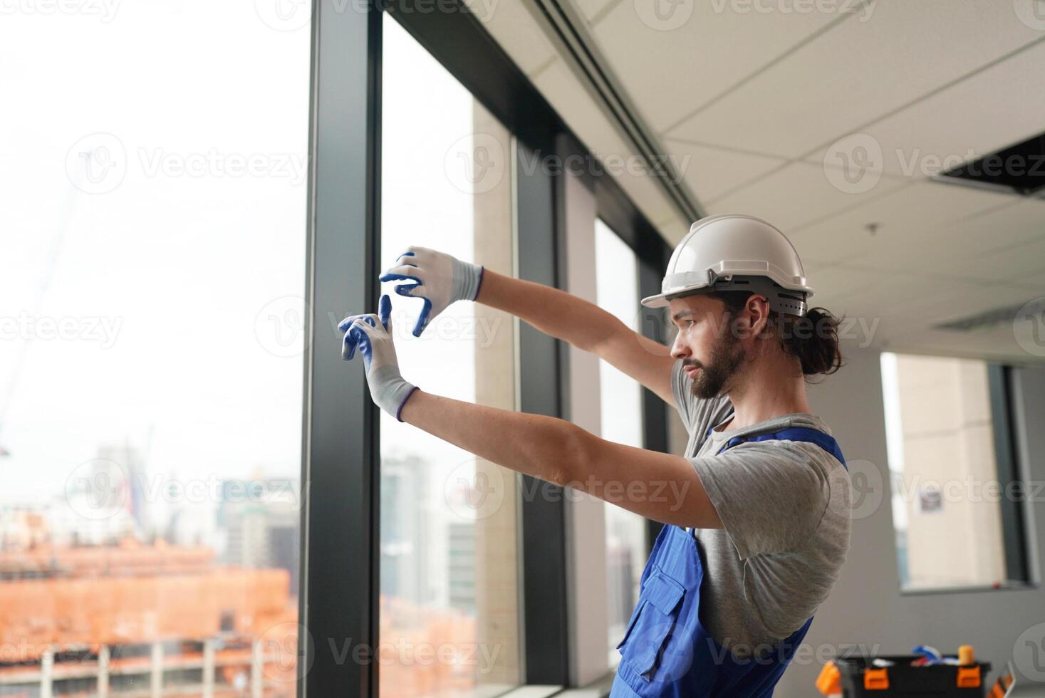 A man in a hard hat and overalls is fixing a window photo