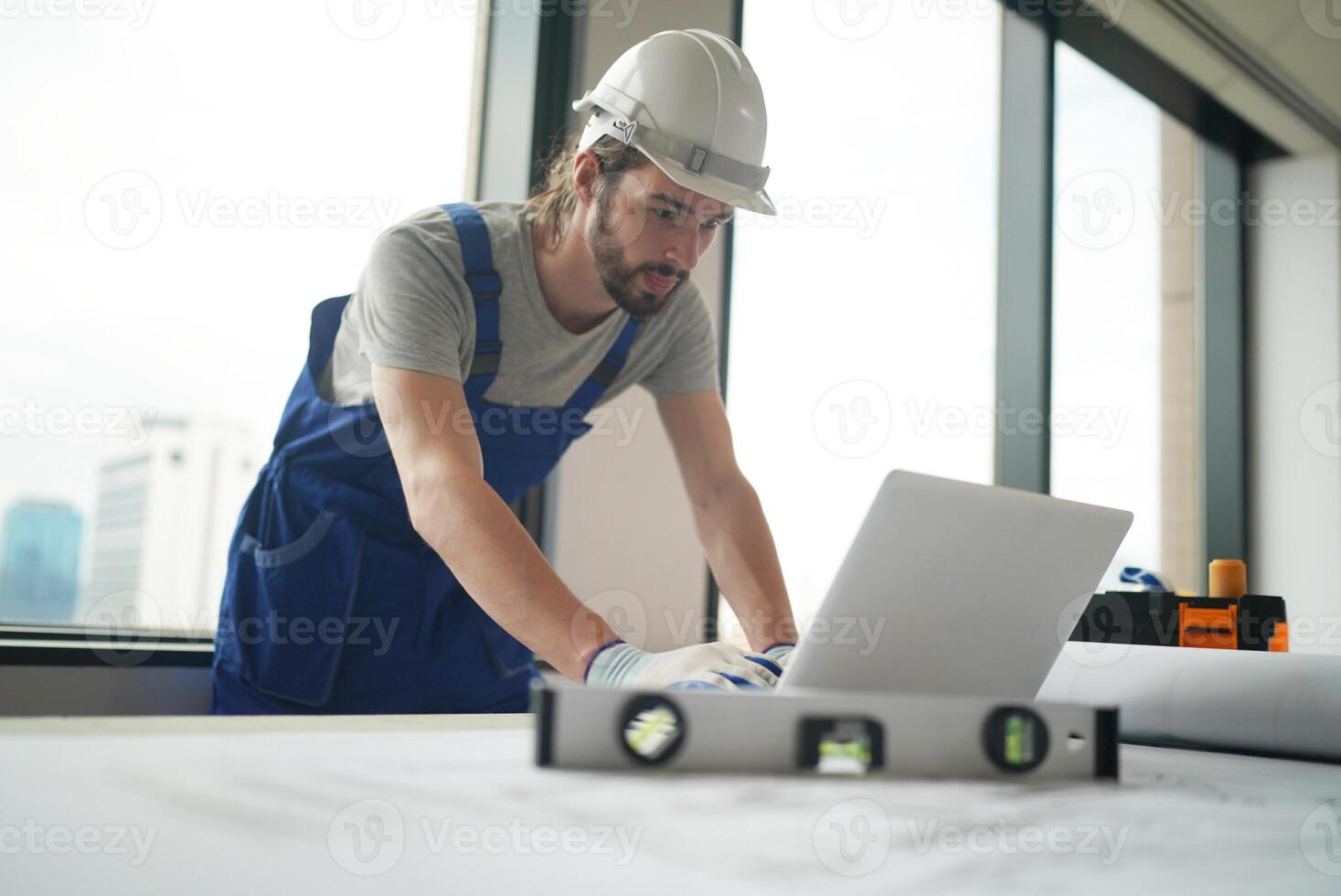 A man in overalls working on a laptop photo