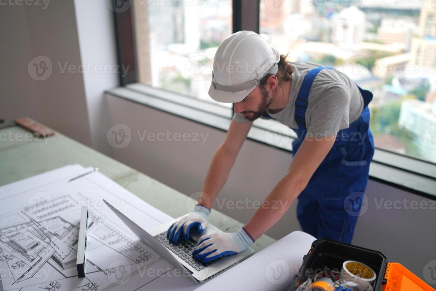 A man in overalls working on a laptop photo