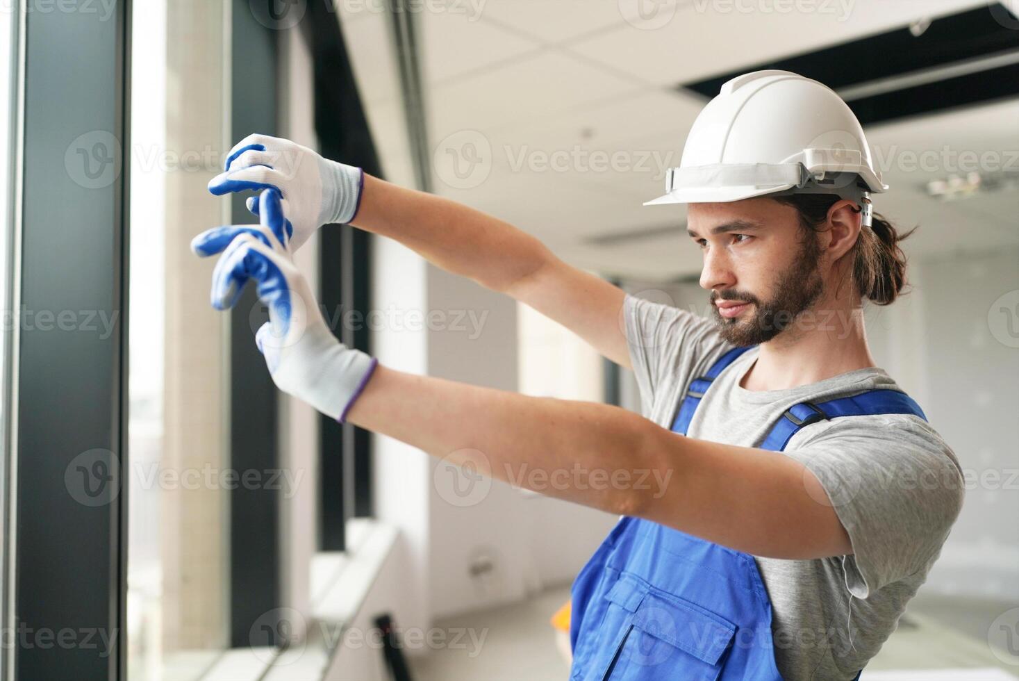 A man in a hard hat and overalls is cleaning a window photo