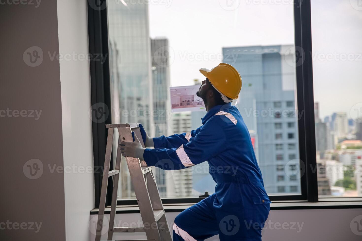 A man in blue overalls is standing on a ladder photo