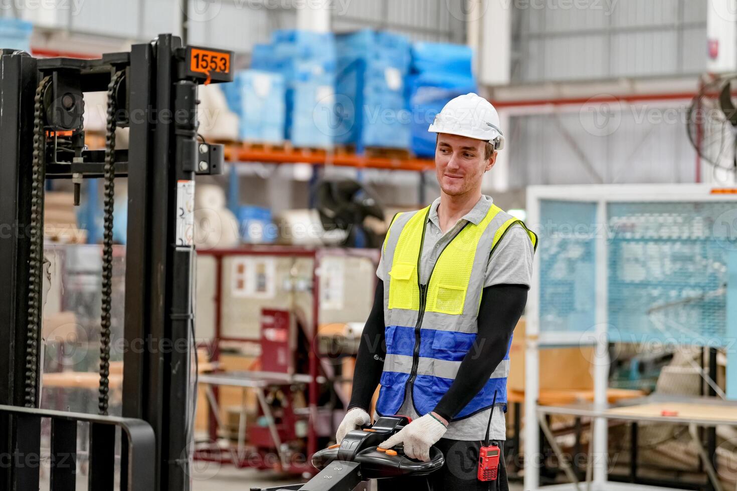 A man in a safety vest and hard hat is standing in front of a forklift photo